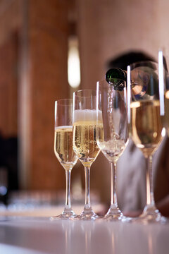 Close-up of a waiter pouring sparkling champagne from a bottle into elegant flutes on a bar counter. Luxury celebration, wedding reception, or banquet event