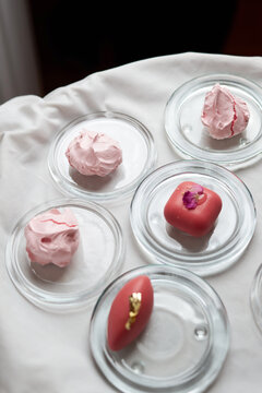 High-angle shot of assorted pink desserts including meringues and glazed petit fours on small glass plates. Elegant gourmet catering for a luxury banquet, wedding, or boutique event