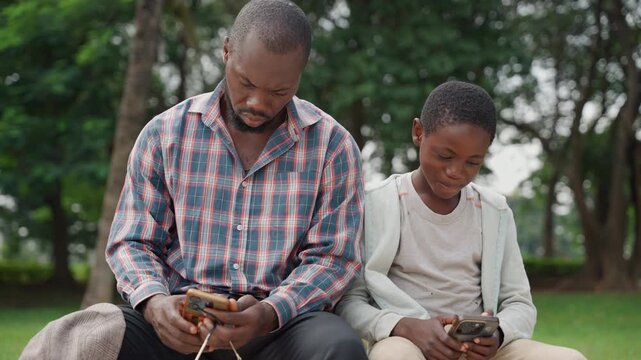 Father and son sharing phone screen on park bench, father demonstrating simple app while son explores game, warm smiles and curious expressions, close interaction, casual clothing, trees and soft