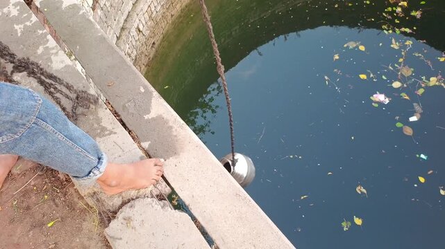 Indian boy pulling a steel pot filled with water from a deep stone well in a rural village