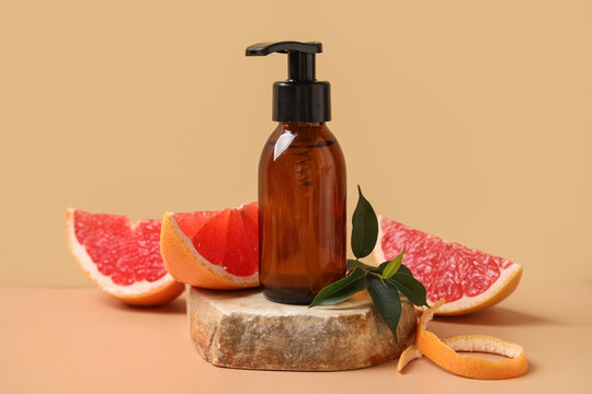 Bottle of cosmetic product, pieces of grapefruit and stone on beige background, closeup