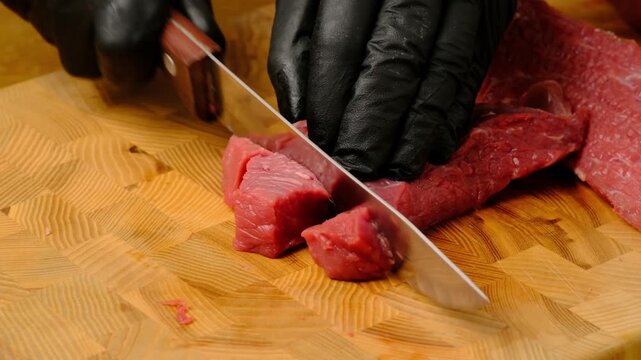 A chef wearing black gloves slices beef flank on a wooden board. Video recipes. Cooking process video.
