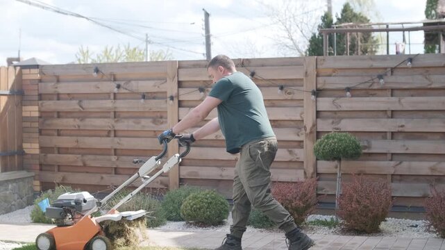 A man uses a professional gasoline scarifier to remove moss and thatch from a green lawn in a private house backyard.