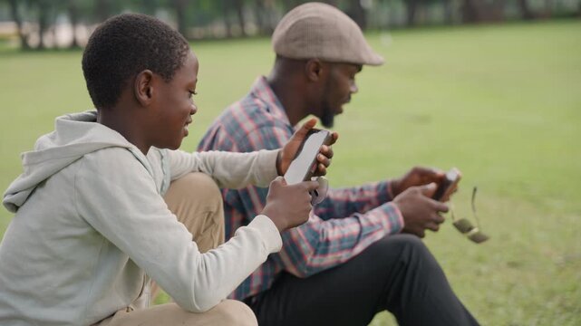 Boy demonstrates phone illusion outdoors. Young boy impresses father with phone magic in park setting. Lively scene of boy surprising father with phone trick during outdoor afternoon