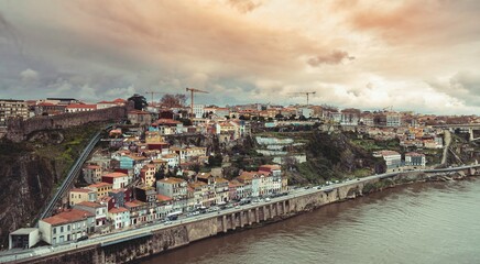 Obraz premium A scenic view of Porto's historic hillside neighborhood reveals colorful buildings along the river. Construction cranes dot the skyline, highlighting urban transformation amidst tourist crowds