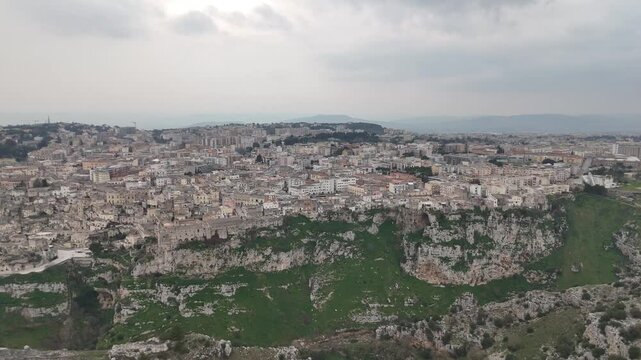 Aerial panorama of an old hilltop town above a rocky ravine under a cloudy sky in southern Italy