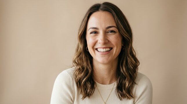 Joyful woman smiling warmly against a soft beige background, natural beauty portrait, approachable expression, clean minimalist styling, flattering light, realistic skin detail, elegant commercial