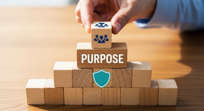 Hand placing teamwork block on purpose pyramid with security shield