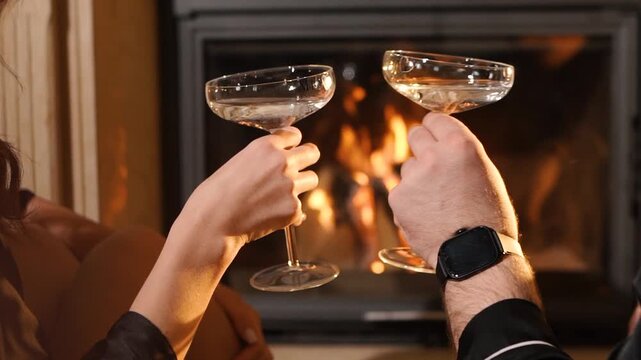 A loving couple on a date drinking an alcoholic cocktail near a fireplace. A man and a woman are having a romantic dinner. A close-up of a glass goblet of champagne. Sparkling wine with reflections