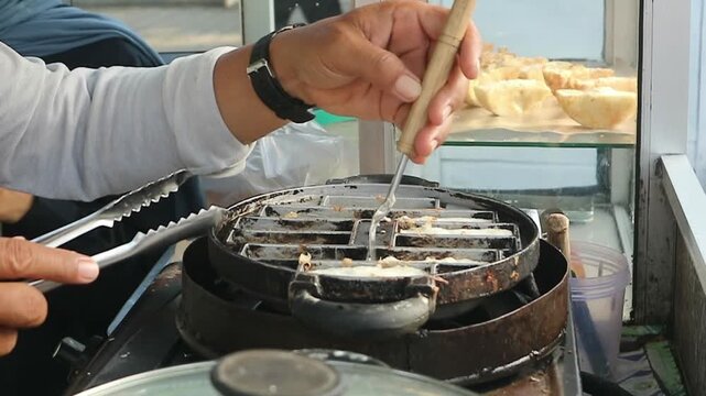 The process of lifting the cooked pancong cake from the pan using a knife and tongs to make it easy to remove from the pan.