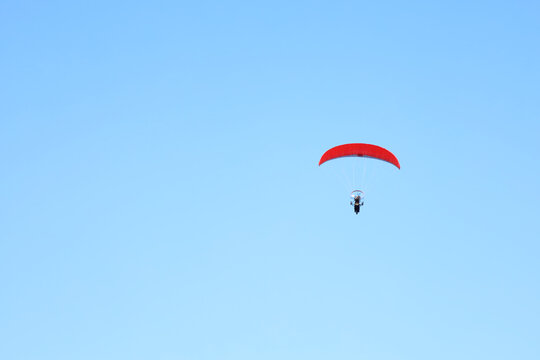 Red parachute soars against vast, clear blue sky