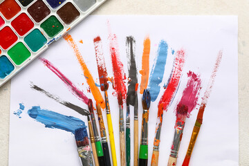 Obraz premium Artist brushes with paint strokes and sheet of paper on white grunge background