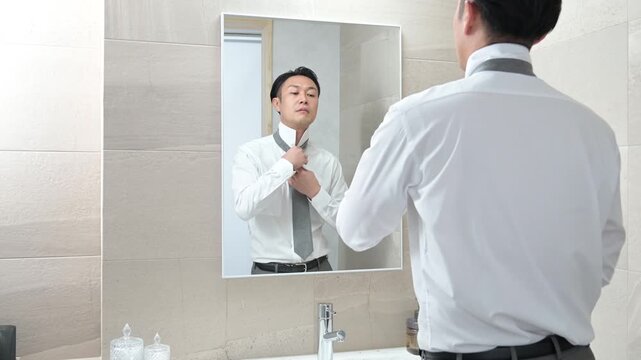 鏡を見てネクタイの結び方に失敗する日本人男性