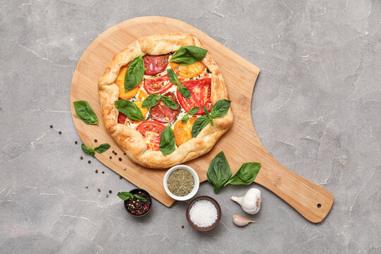 Wooden board with tasty tomato galette with fresh basil and spices on grunge background