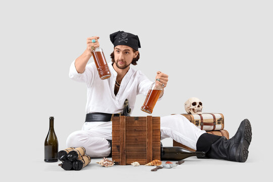 Young pirate with treasure and rum on light background