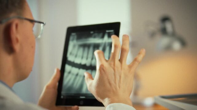 Examining a panoramic X-ray on a sleek touchscreen tablet, the dentist scrutinizes the jaw and teeth, assessing bone health and planning precise treatment in a modern diagnostic workflow