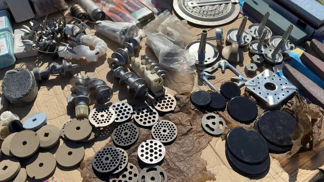 Assorted metal and plastic grinder nozzles laid out on wooden workbench with milling cutter bits round perforated plates dies.