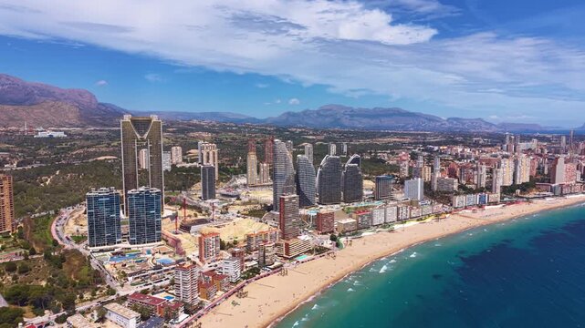 Panoramic aerial view of Benidorm, Spain, showing the iconic skyline with high-rise buildings, sandy beach, turquoise Mediterranean Sea, and mountain backdrop