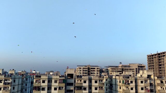 Colorful kites flying over city rooftops during Indian kite festival. Ideal for Makar Sankranti, Uttarayan, cultural celebration, urban lifestyle, and festive atmosphere visuals.