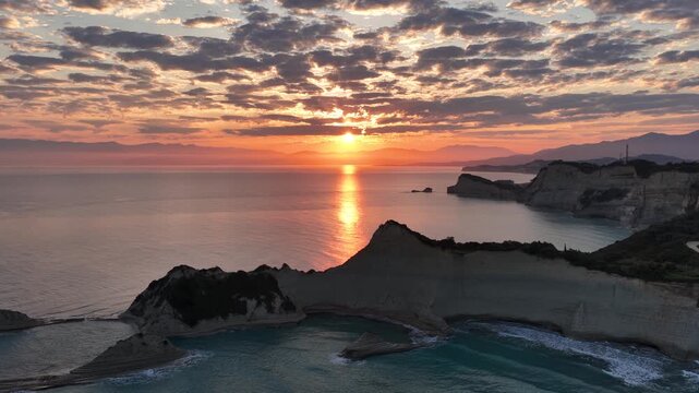 Aerial view of golden sunrise reflecting on the tranquil Ionian Sea behind unique rock formations of Cape Drastis in Corfu Island Greece, breathtaking coastal landscape scenery