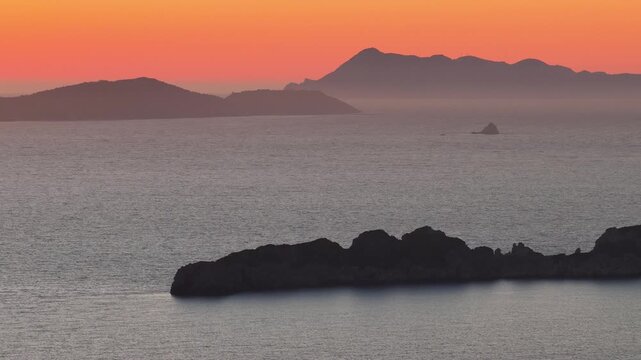 Dramatic sunset silhouettes of the Diapontia Islands over the calm Ionian Sea, viewed from Afionas, Corfu, Greece. Beautiful orange dusk sky landscape