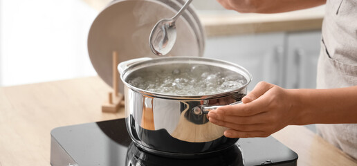 Woman and stainless steel pot with boiling water on stove in kitchen, closeup