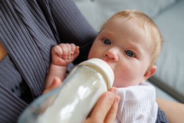 Fototapeta premium Close-up of a baby drinking milk from a bottle while being held by a parent