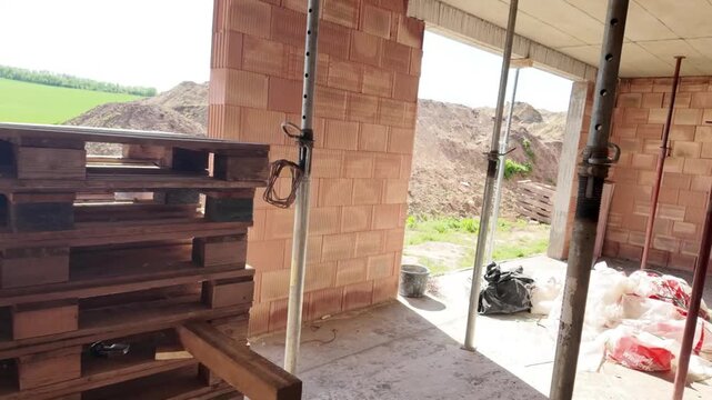 Construction site interior with brick walls and support poles, progress view. Interior view of a building under construction, showcasing unfinished brick walls, scaffolding poles, and stacked wooden