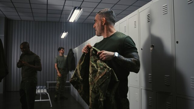 Three Diverse Athletic Soldiers in Military Uniforms Undress by Lockers, Friendly Interacting and Chatting After Successfully Finishing Mission or Duty. Concept of Shift End on Modern Military Base.
