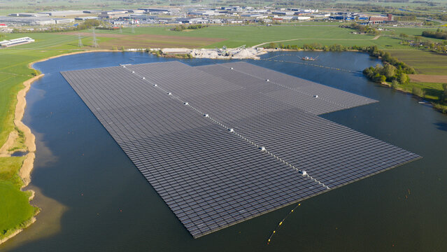 Aerial view of the Bomhofsplas floating solar farm with thousands of photovoltaic panels on a lake surrounded by green fields and industrial areas Zwolle, Overijssel, Netherlands.