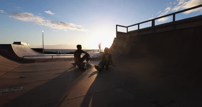 Young friends chatting at skateboard city park during summer sunset time - Gen z people lifestyle and extreme sport concept - UGC wide lens content