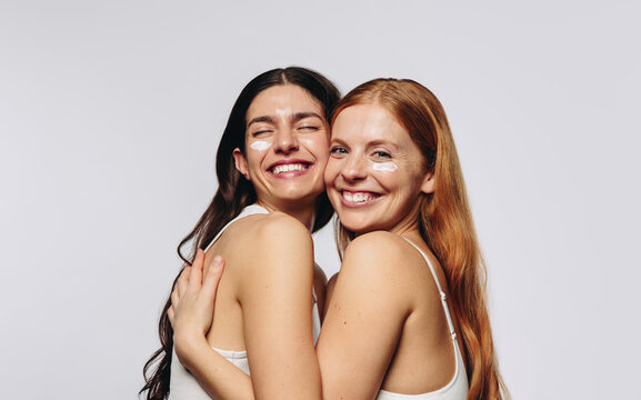 Two women hugging and smiling with eye cream