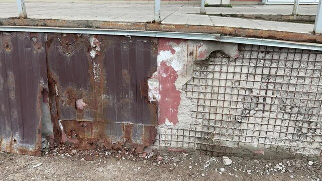 Rusty metal cladding and mesh on apartment extension showing heavy corrosion, flaking paint and exposed brick, twisted mesh.