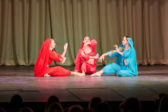 Three dancers in vibrant traditional odalisque costumes performing storytelling dance on stage