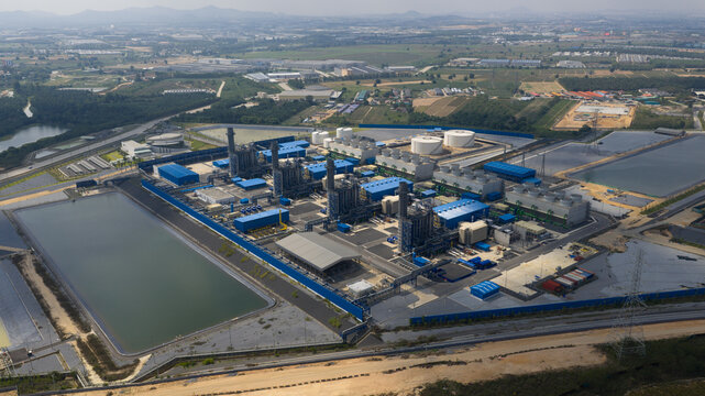 Aerial view of Sriracha Power Plant GSRC featuring blue industrial buildings, cooling towers, and large water reservoirs under a hazy sky in Tambon Khao Khan Song, Chang Wat Chon Buri, Thailand.