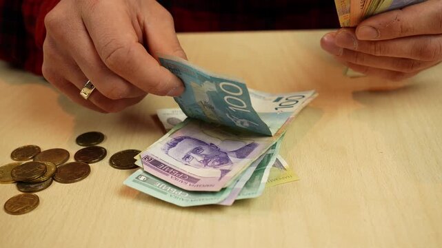 Hands count and place mixed Serbian dinar banknotes on a table with coins. Cash handling and budget tracking concept for finance, savings, spending and daily money management