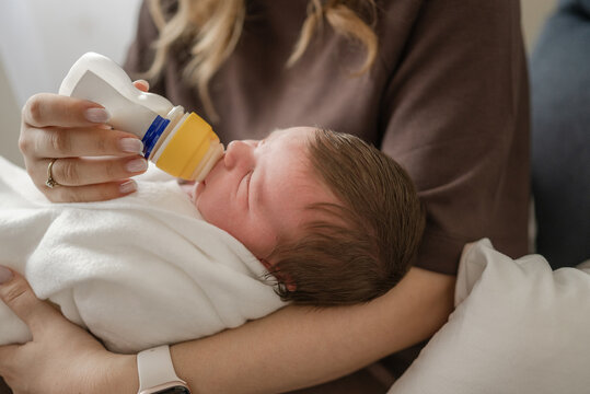 Close-Up Of A Newborn Eating From A Bottle In The Mother's Arms