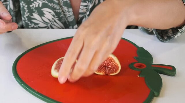Female hands portioning ripe figs front view on cutting board, dividing soft fruit into segments for serving or garnish in home kitchen, simple food preparation with fresh seasonal ingredients