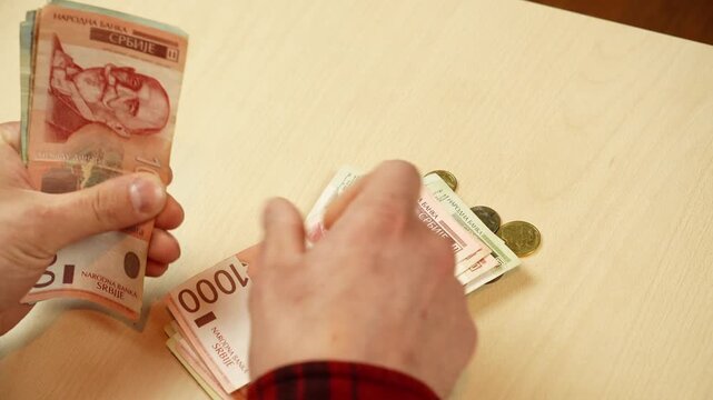 Hands count Serbian dinar bills and coins on a table with mixed denominations. Cash budgeting and expense control concept for savings, payments, accounting and personal finance