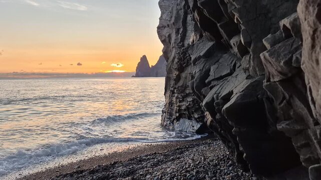 Ocean Cliffs Sunset, waves gently lap a rocky beach at the base of dramatic cliffs, golden hour light bathes the tranquil sea, creating a serene coastal landscape