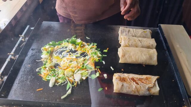 Close up of Kottu Roti being prepared on a hot metal griddle in Ella, Sri Lanka, chopped flatbread mixed with vegetables, egg and curry, street food cook skillfully chopping and blending ingredients