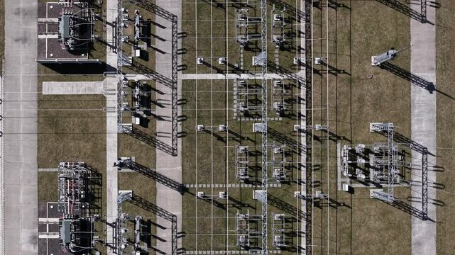 An aerial top-down view shows the intricate geometric layout of a high voltage electrical substation distributing power across the grid.