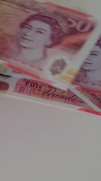 A hand drops a &pound;50 note onto a white surface then methodically counts out a full &pound;1,000 in polymer &pound;50 notes, carelessly building a loosely stacked, dishevelled pile in slow motion. Vertical format.