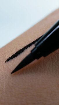 Black eyeliner swatches on skin with a wide stroke in close up, showing broad swipe and natural skin texture, suitable for beauty themes and face makeup product presentation.