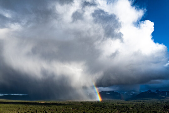 Aerial view of Cairngorms National Park with a dramatic rain cloud and a bright rainbow over the dense forest and distant mountains Scotland, United Kingdom.