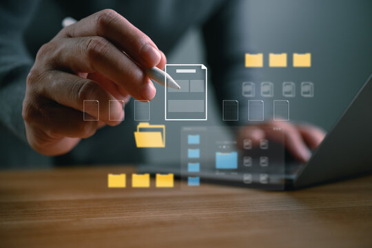 Close-up of hand using stylus on laptop with virtual file and folder icons, illustrating document management, digital archive, cloud storage, data organization, and paperless workflow technology.
