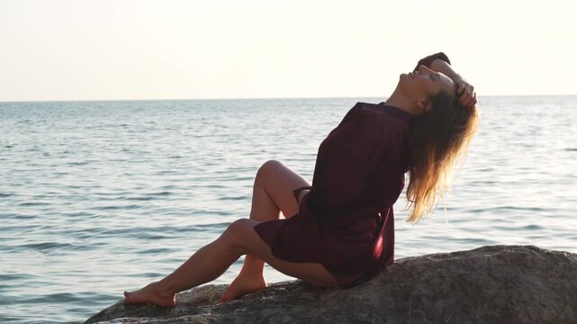 Woman sea rock sitting on a large boulder by the ocean at sunset enjoying the calm water and refreshing sea breeze