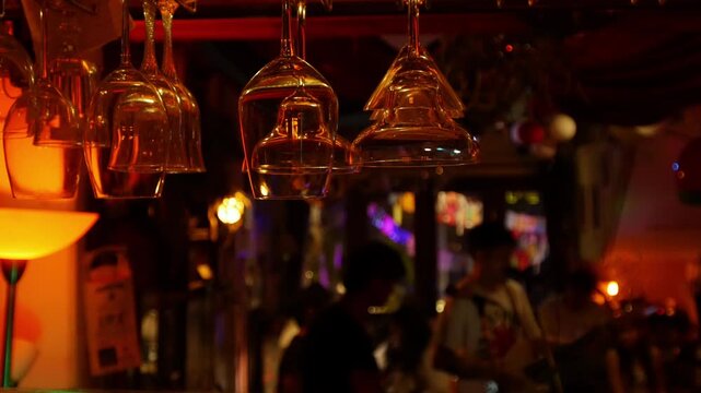 Wine glasses hanging upside down from bar ceiling rack with live music band performing in bokeh background at night