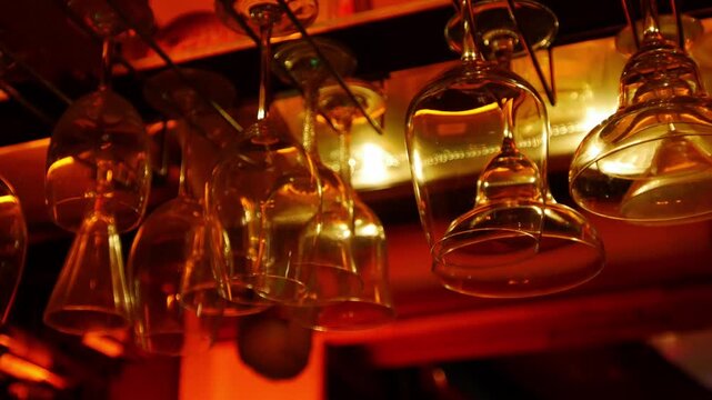 Wine glasses hanging upside down on rack above bar shelf with warm golden amber lighting elegant restaurant interior