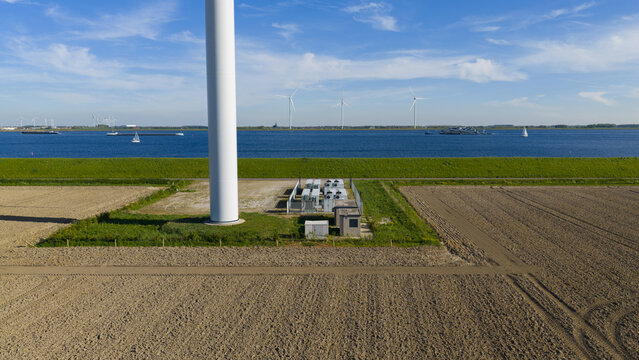 Aerial view of Mariadijk wind turbine base and electrical infrastructure next to plowed fields and the Volkerak waterway Ooltgensplaat, Zuid-Holland, Netherlands.